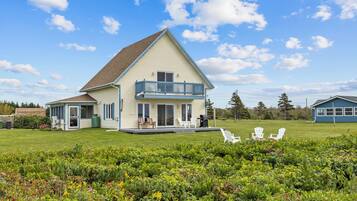 A two-story house with a balcony, a covered porch, and a grassy yard with outdoor seating.