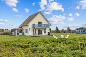 A two-story house with a balcony, a covered porch, and a grassy yard with outdoor seating.