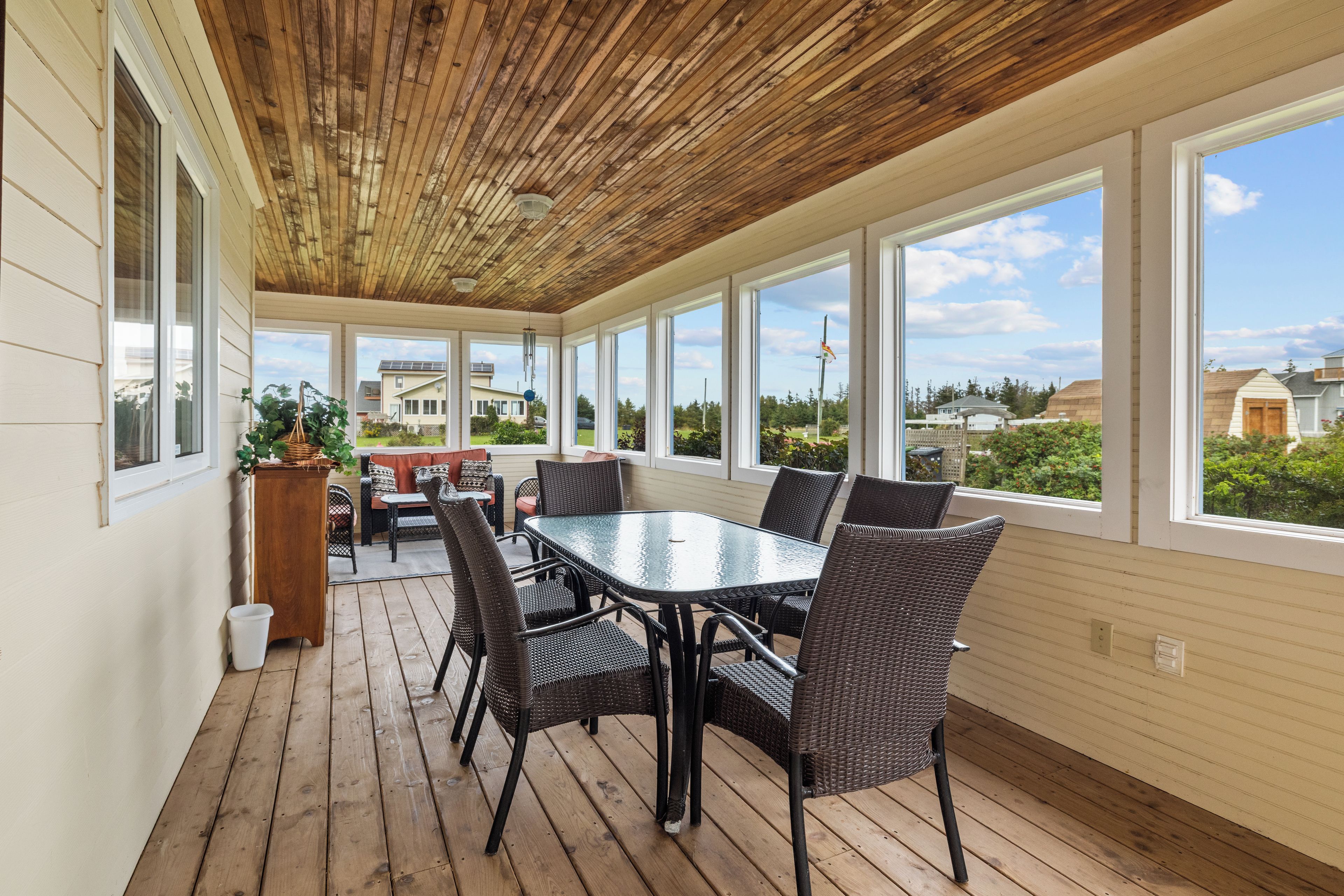A covered patio with a glass table and wicker chairs, overlooking a residential area.
