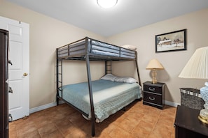 A bunk bed in a room with a door, a lamp, a picture on the wall, and a small table.