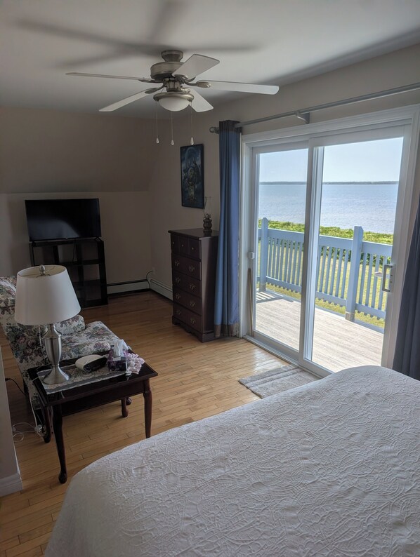 A bedroom with a bed, a television, a dresser, and a view of the sea through a sliding door.