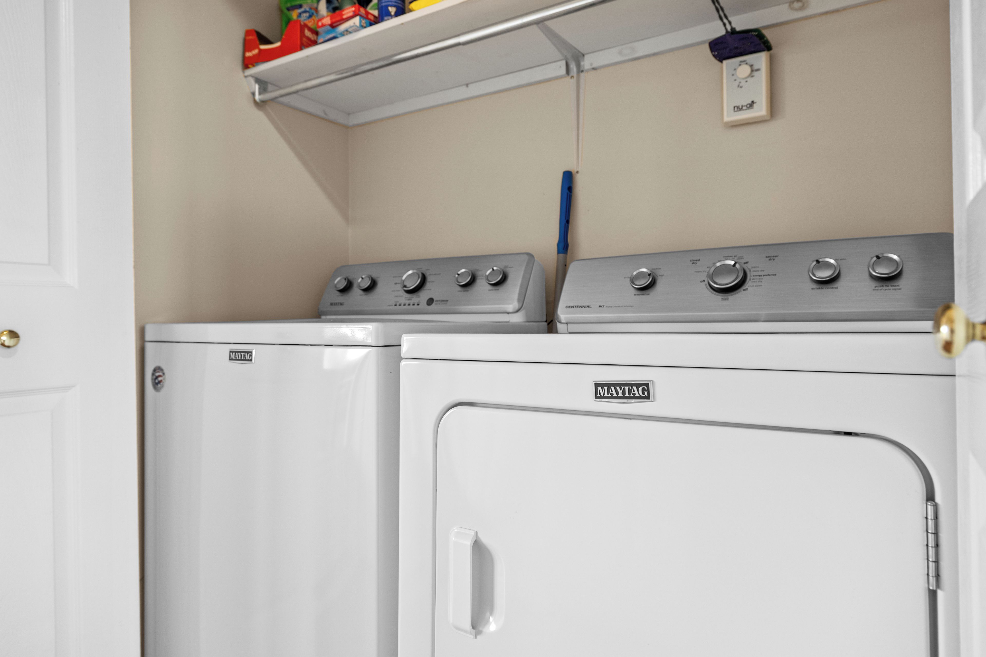 Ein Waschraum mit zwei Maytag Waschmaschinen und Trocknern, einem Regal mit diversen Gegenständen und einer Steckdose mit Stecker.