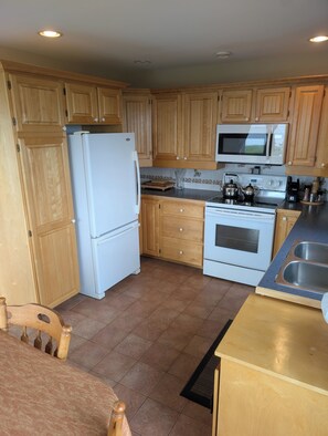 A kitchen with wooden cabinets, a white refrigerator, a microwave, a stove, and a sink.