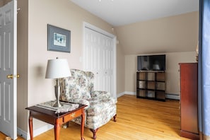 A living room with a floral armchair, a wooden coffee table, a television stand, and a wardrobe.