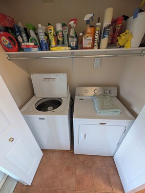 Une buanderie équipée de deux machines à laver Maytag, d’une étagère contenant des produits de nettoyage et d’une serviette posée sur le sèche-linge.
