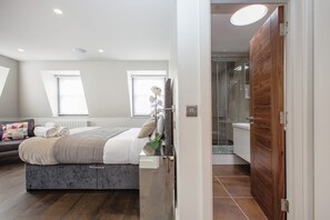 A modern bedroom with a bed, a bedside table, a window, and a bathroom visible through an open door. - Spacious 2BR Penthouse with Private Terrace - Soho (London)