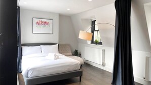 Quarto moderno com cama, luminária de cabeceira, radiador e janela com cortinas.