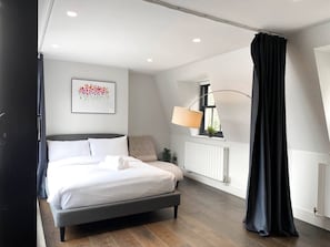 Ein modernes Schlafzimmer mit Bett, Nachttischlampe, Heizkörper und einem Fenster mit Vorhängen.