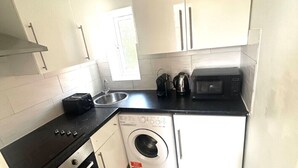 A compact kitchen with a stove, microwave, and built-in washing machine. - Stylish Central London apartment is next to the tube Chelsea border (London)