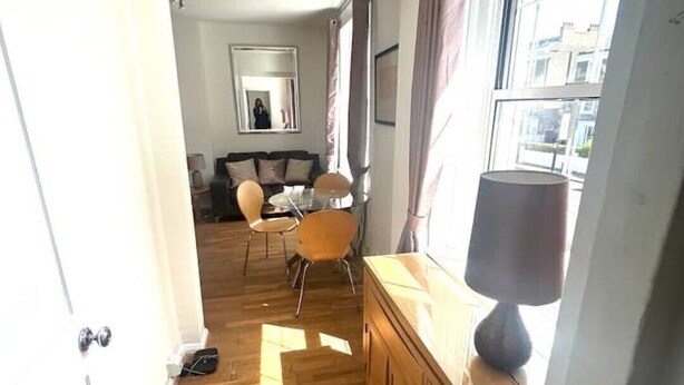 A narrow hallway with wooden flooring leading to a dining area with a table and chairs. - Stylish Central London apartment is next to the tube Chelsea border (London)