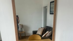 A room with a wooden table and a single chair, a mirror reflecting the room, and a sofa with cushions. - Stylish Central London apartment is next to the tube Chelsea border (London)