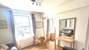 A living room with a sofa, a coffee table, and a dining area with chairs and a table. - Stylish Central London apartment is next to the tube Chelsea border (London)