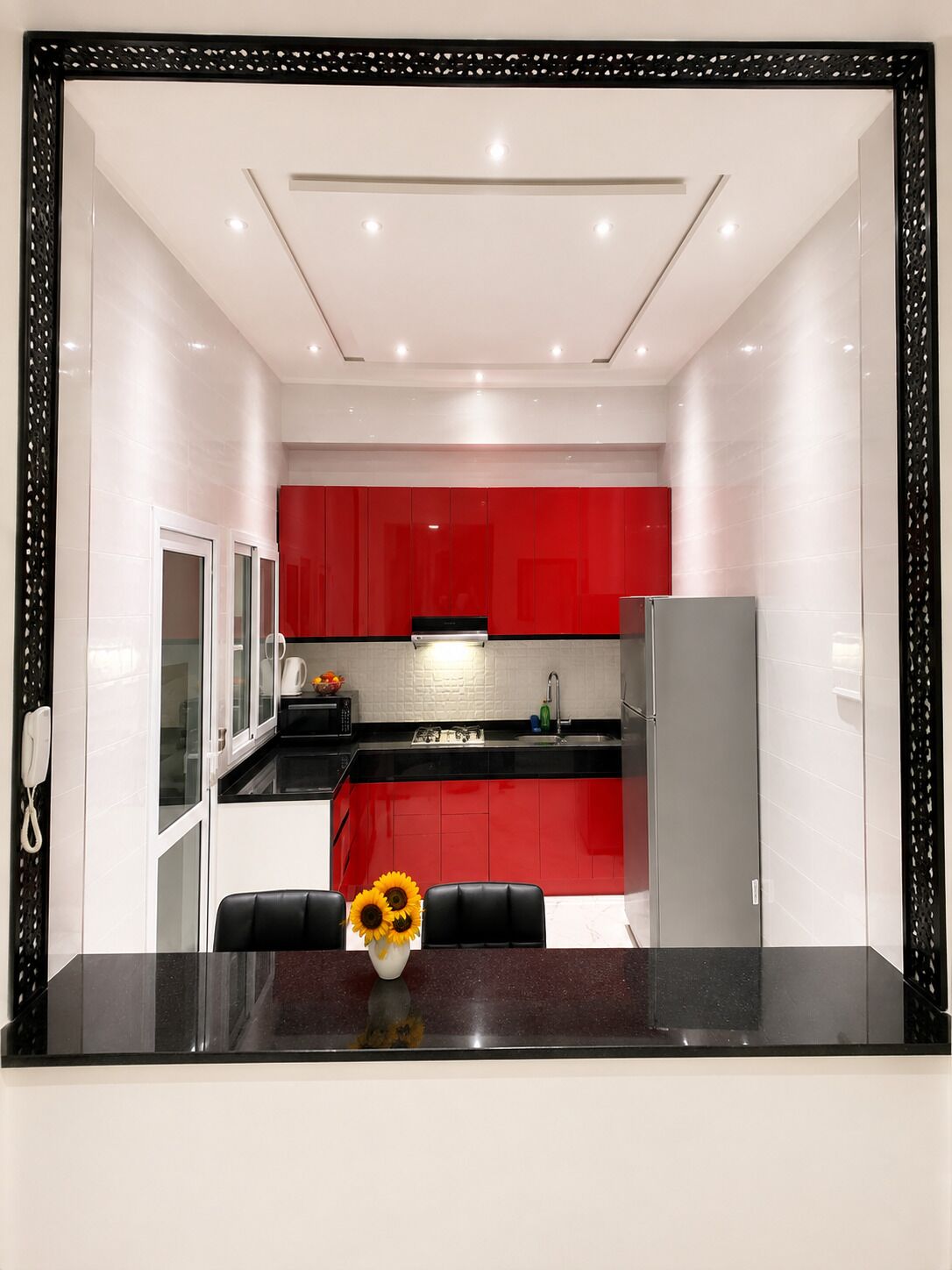 A modern kitchen with red cabinets, a black countertop, and a white backsplash.