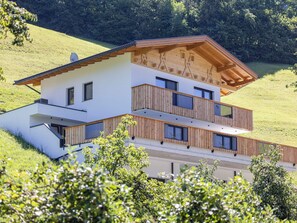 Une maison moderne à deux étages, dotée d’un toit en pente, de balustrades en bois sur le balcon et d’une façade blanche.
