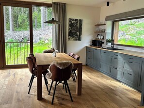 Eine moderne Küche mit einer großen Kochinsel, Holzböden und Blick auf eine bewaldete Gegend.
