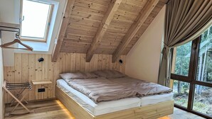 A bedroom with a sloped ceiling, a bed with a headboard, a window with curtains, and a wooden floor. - Nice apartment for 5 guests with WIFI, TV and balcony (Jilemnice)
