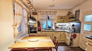 Uma cozinha com uma mesa de madeira, cadeiras, um fogão e uma janela com cortinas.