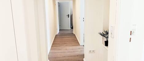 A hallway with wooden flooring, white walls, and a door at the end.