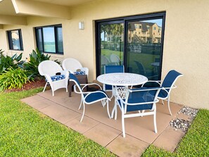 An outdoor patio with a round table and six chairs, surrounded by a well-maintained lawn and a building with large windows. - Sunshine Beach Retreat at Summerhouse - Ground Floor, Heated Pools, Beach Access (St. Augustine)