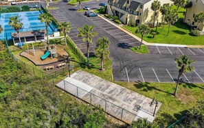 A parking lot with a playground, palm trees, and a building with a sloped roof. - Sunshine Beach Retreat at Summerhouse - Ground Floor, Heated Pools, Beach Access (St. Augustine)