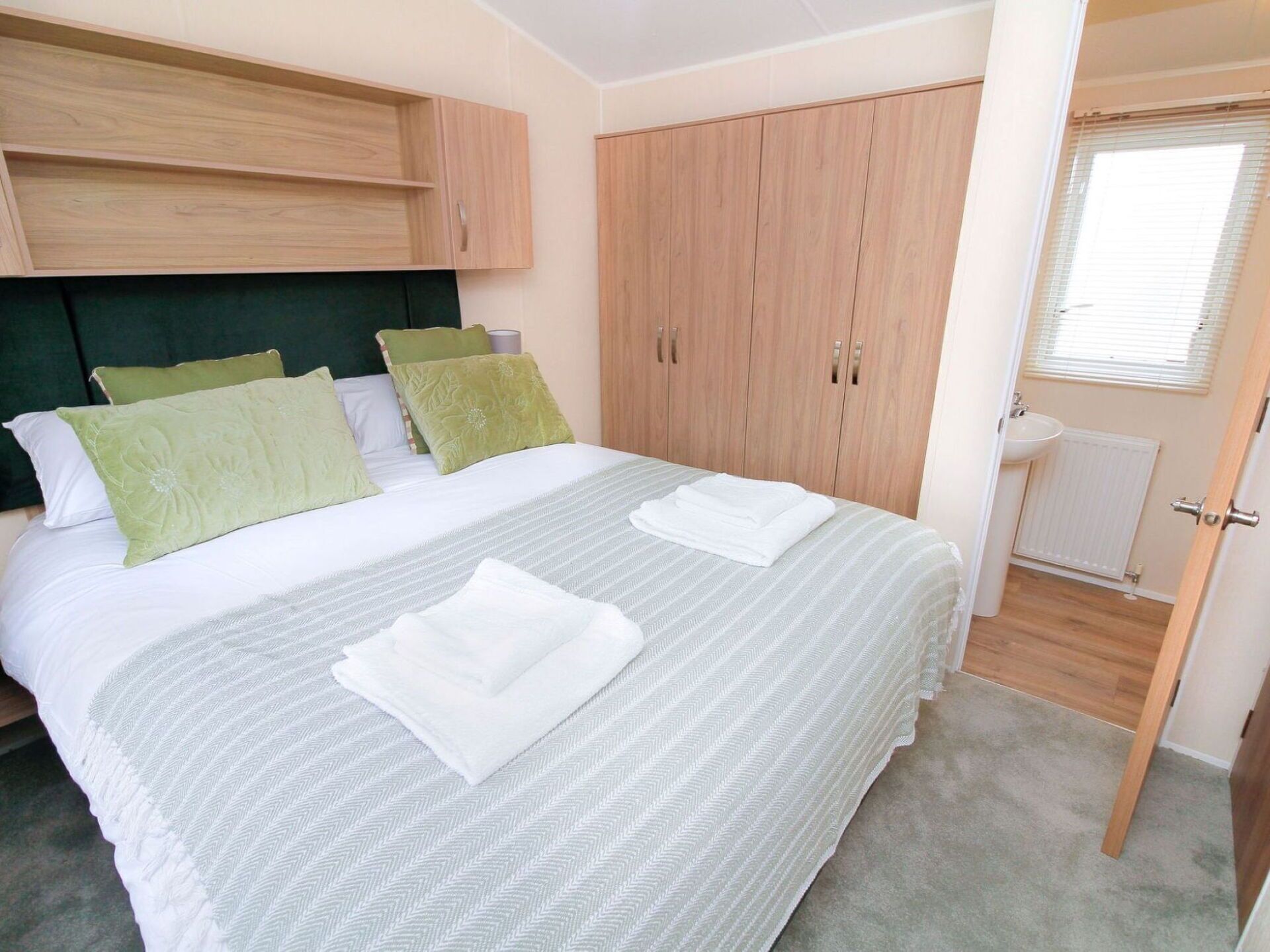 A bedroom with a bed, green pillows, a wooden wardrobe, and a bathroom with a sink and toilet.