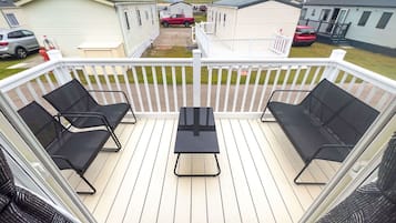 Una terraza con dos sillones reclinables negros y una mesa central, rodeada por una valla blanca.