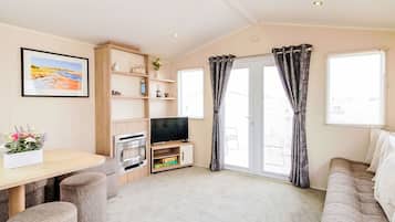 Ein Wohnzimmer mit einer Couch, einem Fernseher, einem Kamin, einem Esstisch und einem Fenster mit Vorhängen.