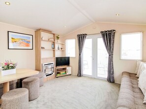 A living room with a sofa, a TV, a fireplace, a dining table, and a window with curtains.