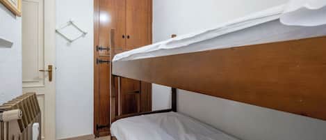 A small, single-bed room with a wooden headboard, a radiator, a wardrobe, and a door with a light fixture above it.