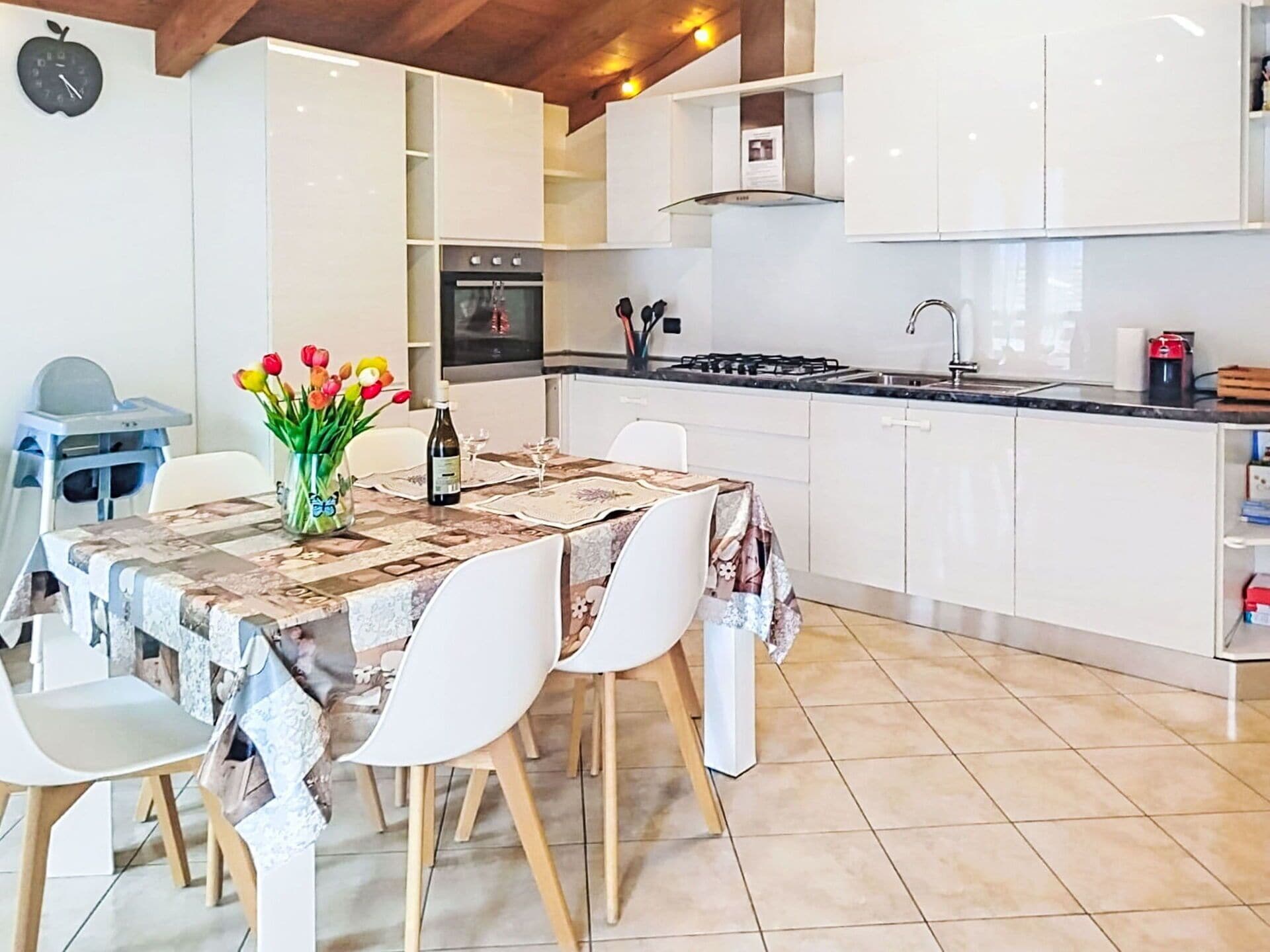 Una cucina moderna con mobili bianchi, un tavolo da pranzo con sedie e un vaso di tulipani.