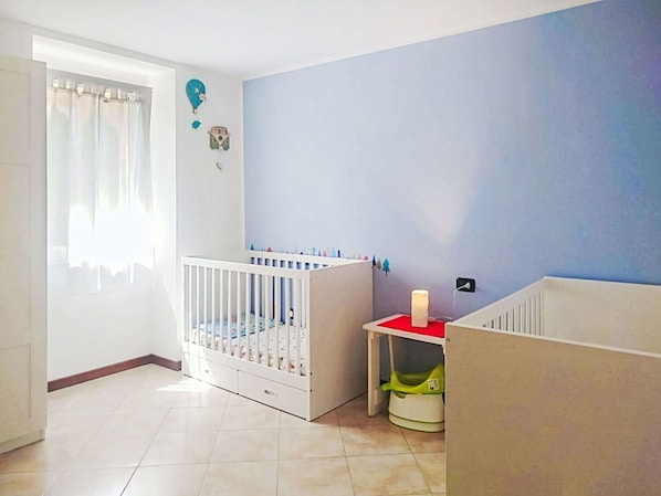 Ein Zimmer mit einem Babybett, einem kleinen Tisch mit roter Oberfläche und einer Wand mit blauem Akzent.