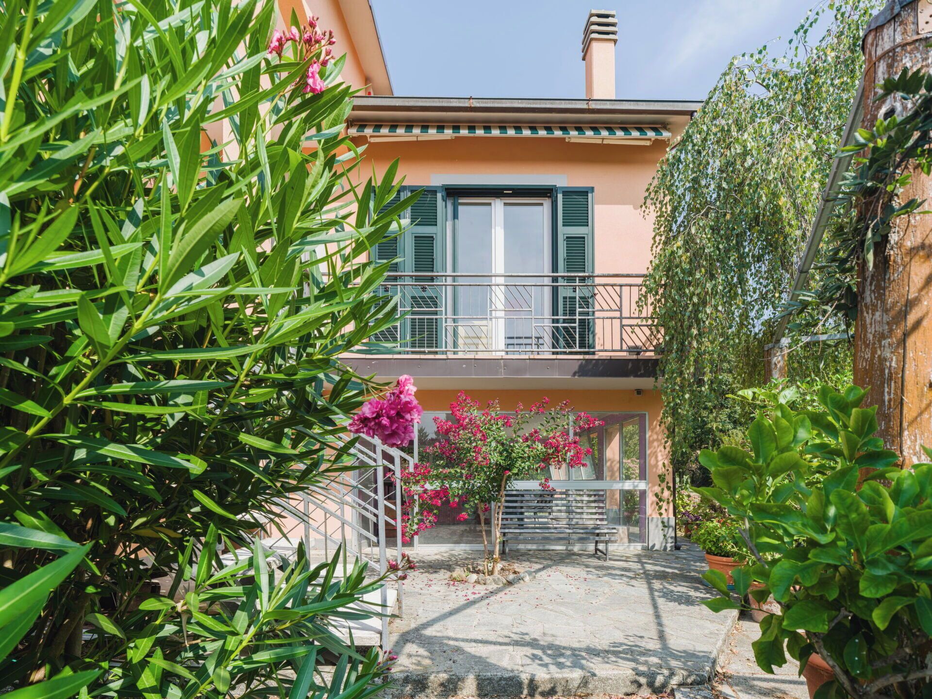 Ein Wohngebäude mit Balkon, Treppe und umgebender Bepflanzung.