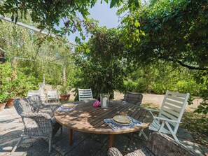 Un patio al aire libre con una mesa redonda de madera, sillas de mimbre y una silla blanca.