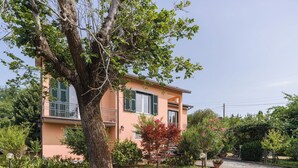 A two-story house with a balcony, surrounded by a well-maintained garden and a large tree.