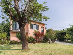 A two-story house with a balcony, surrounded by a well-maintained garden and a large tree.
