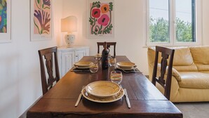 A dining area with a wooden table set for four, surrounded by chairs, a sofa, and artwork on the walls.