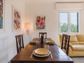 A dining area with a wooden table set for four, surrounded by chairs, a sofa, and artwork on the walls.