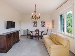 A living room with a dining table, chairs, a sofa, a TV, and artwork on the walls.