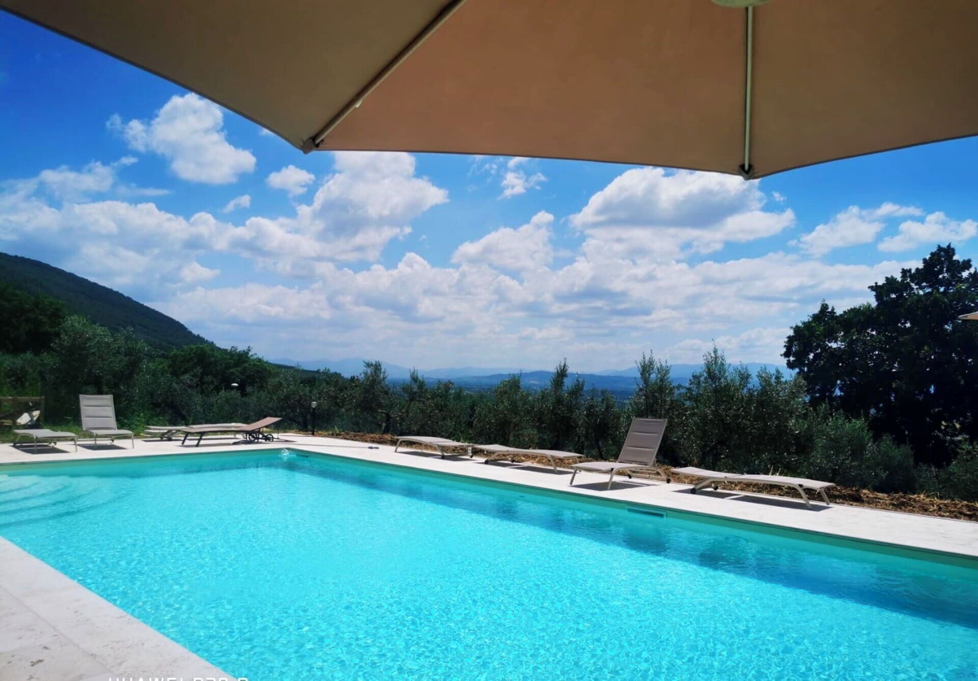 A clear blue pool with lounge chairs and a canopy, surrounded by greenery and mountains.