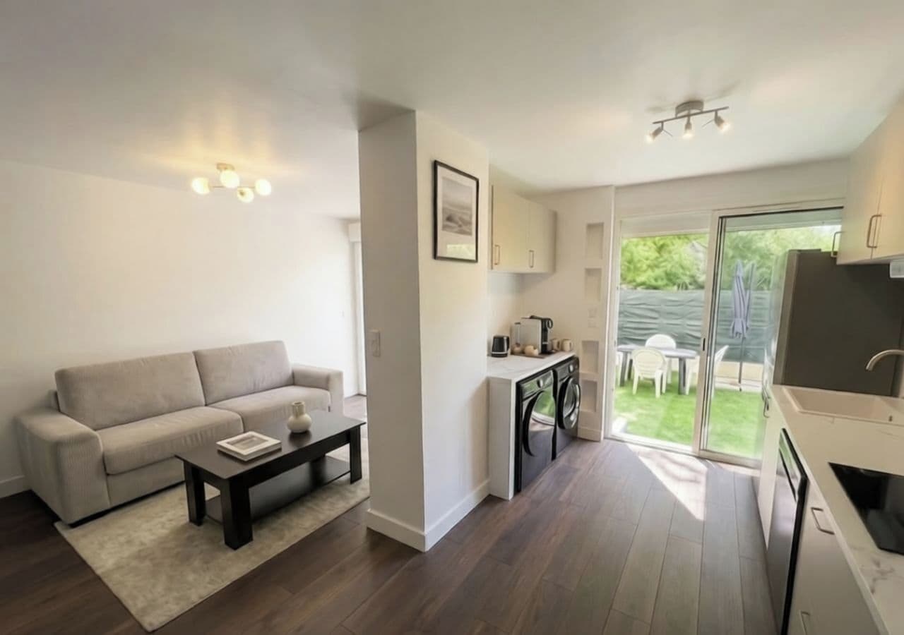 A modern living room with a sofa, coffee table, and a small kitchen area with a washing machine.