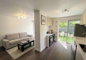 A modern living room with a sofa, coffee table, and a small kitchen area with a washing machine. - 5 minutes from the beaches!! Cosy apartment with garden. (Hyères)