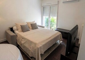 A bedroom with a bed, a television, and a window with blinds. - 5 minutes from the beaches!! Cosy apartment with garden. (Hyères)