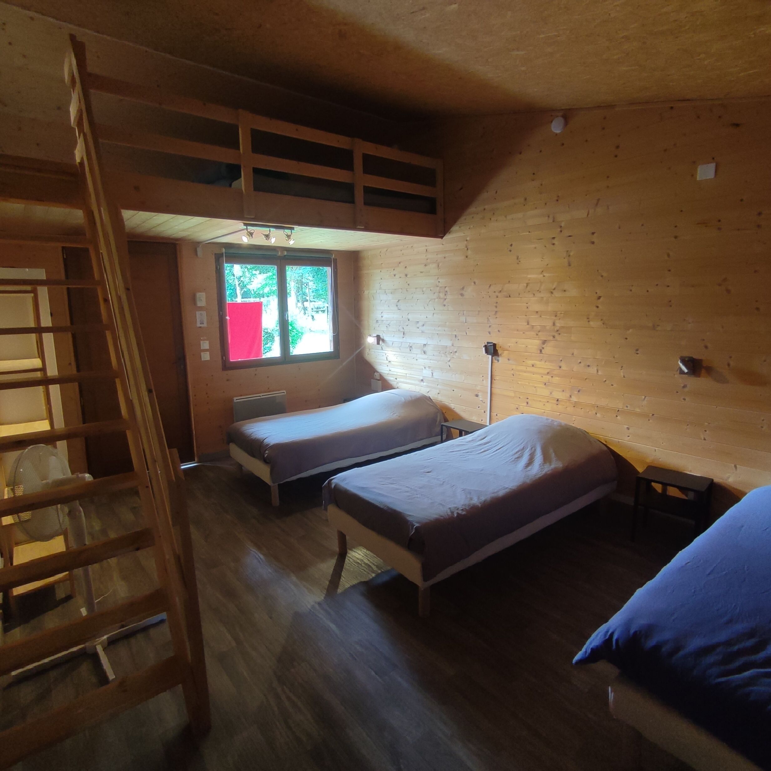 A room with two beds, a wooden ladder, and a window with a red cloth.
