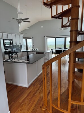 A modern kitchen with a central island, wooden flooring, and a view of the ocean through large windows. - Dune Road Oceanfront (Westhampton Beach)