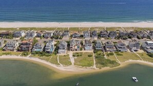 Ett bostadsområde vid kusten med hus längs stranden, en båt på vattnet och fri utsikt över havet.