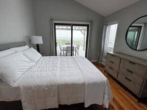 A bedroom with a bed, a dresser, a mirror, and a view of the outdoors.