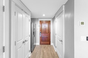 Ein Flur mit weißen Türen, eine Holztür am Ende und ein Thermostat an der Wand.