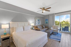 A hotel room with a large bed, a ceiling fan, a balcony with outdoor furniture, and artwork on the walls. - Grand Sandestin 2402 | Newly Renovated Studio | New to Program (Miramar Beach)