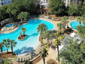 A large outdoor swimming pool with multiple sections, surrounded by palm trees and lounge chairs. - Grand Sandestin 2402 | Newly Renovated Studio | New to Program (Miramar Beach)