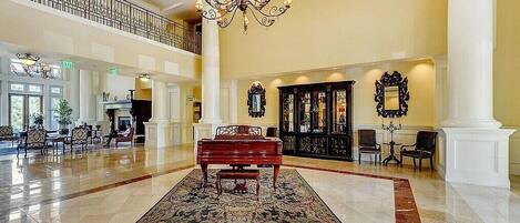 A grand lobby with a piano, chandeliers, and a high ceiling.
